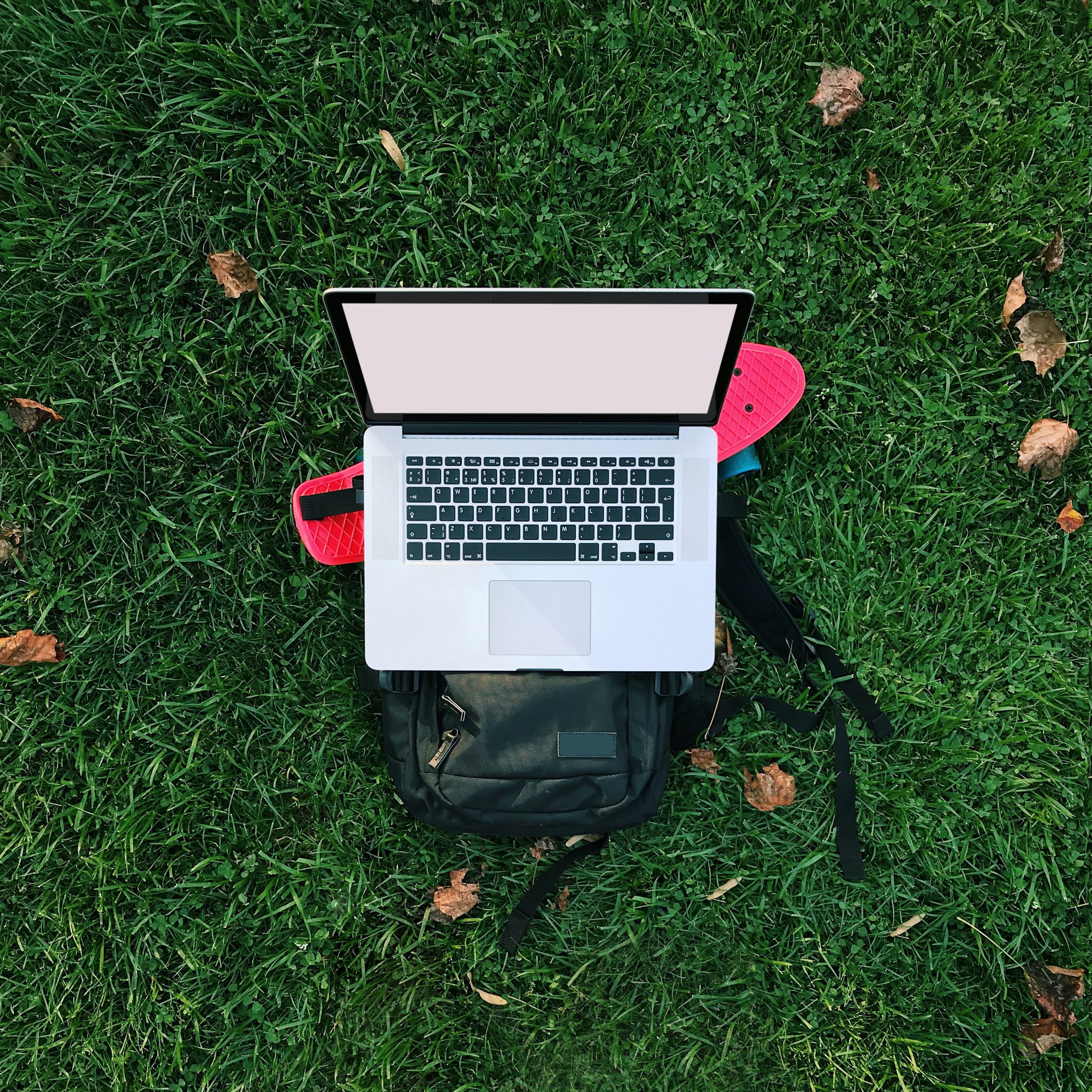 Laptop on top of skateboard and backpack on grass background